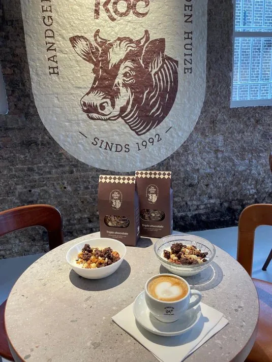 Coffee, chocolate and De Bonte Koe bags on a café table under the cow logo.