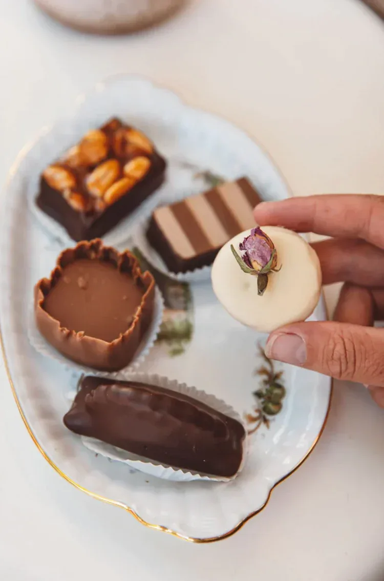 A hand taking a praline from a plate of De Bonte Koe chocolates.