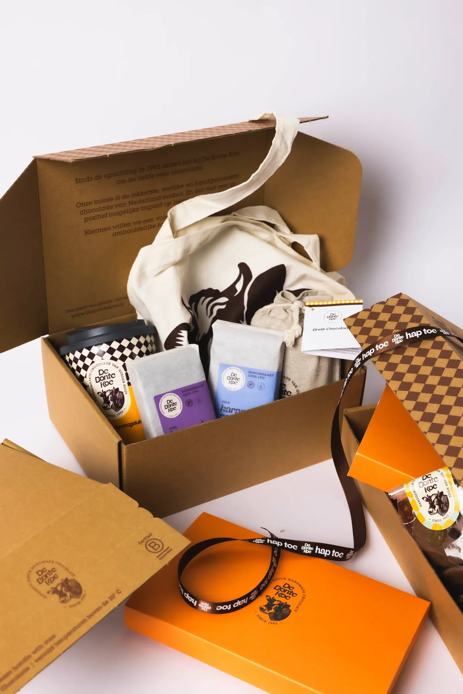 An opened De Bonte Koe gift box: a tote bag, a coffee cup, chocolate and branded packaging.