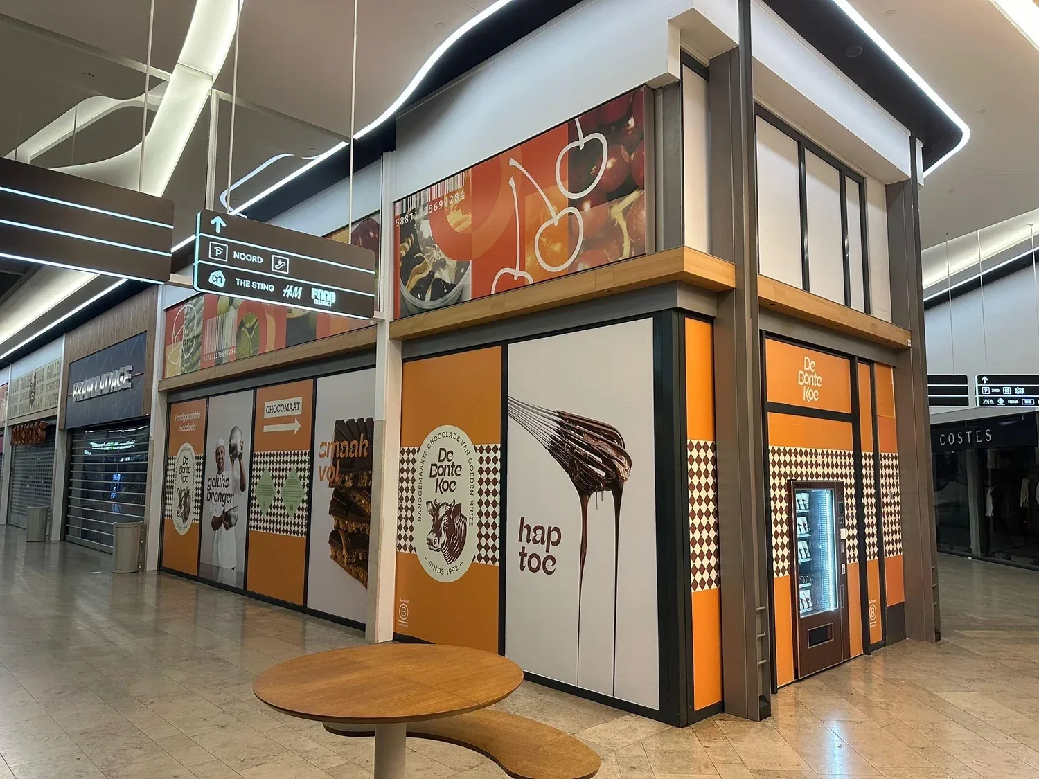 A De Bonte Koe shop in a shopping centre, with a chocolate vending machine built into its orange front.