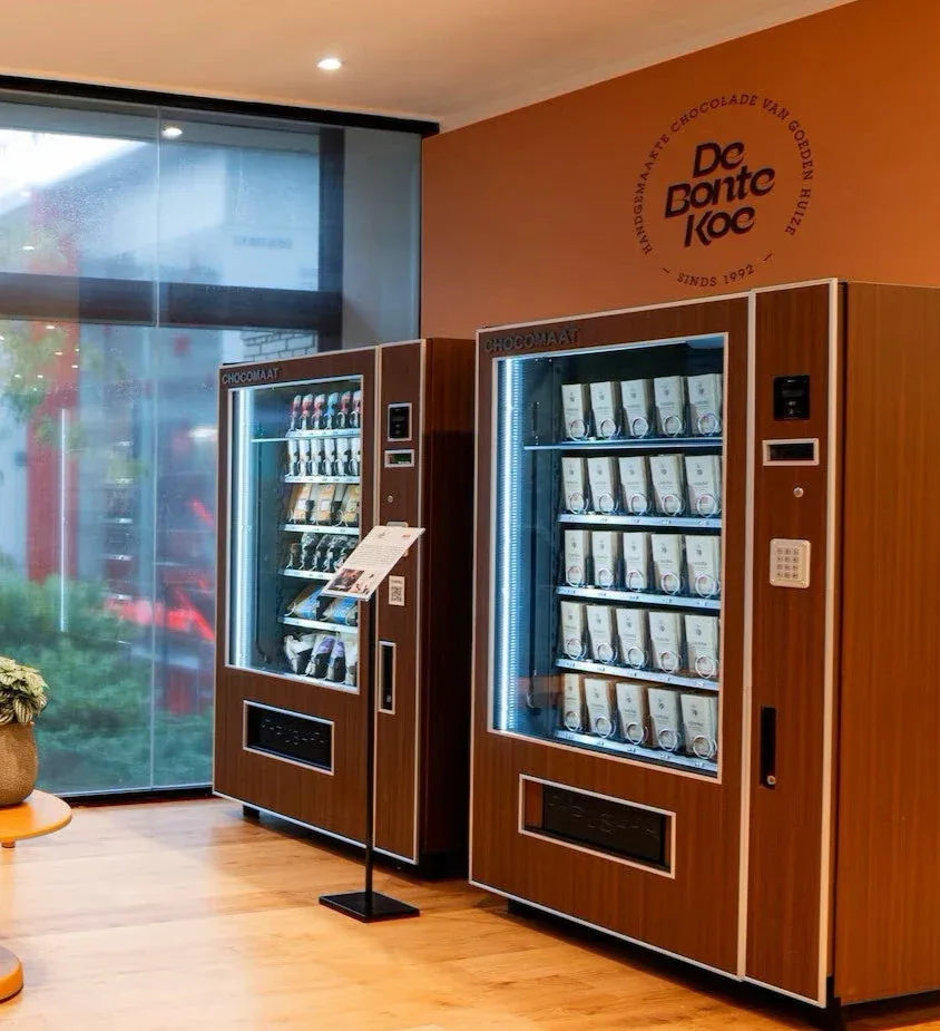 Two De Bonte Koe vending machines side by side in a bright lobby.