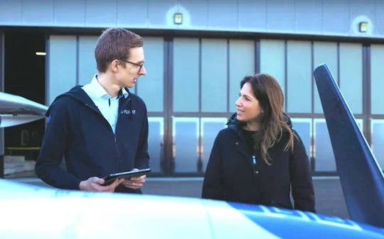 Two people talking beside an E-Flight Academy plane, one holding a tablet.