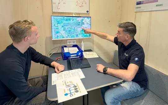 An instructor pointing at a flight map on a screen, briefing a student.