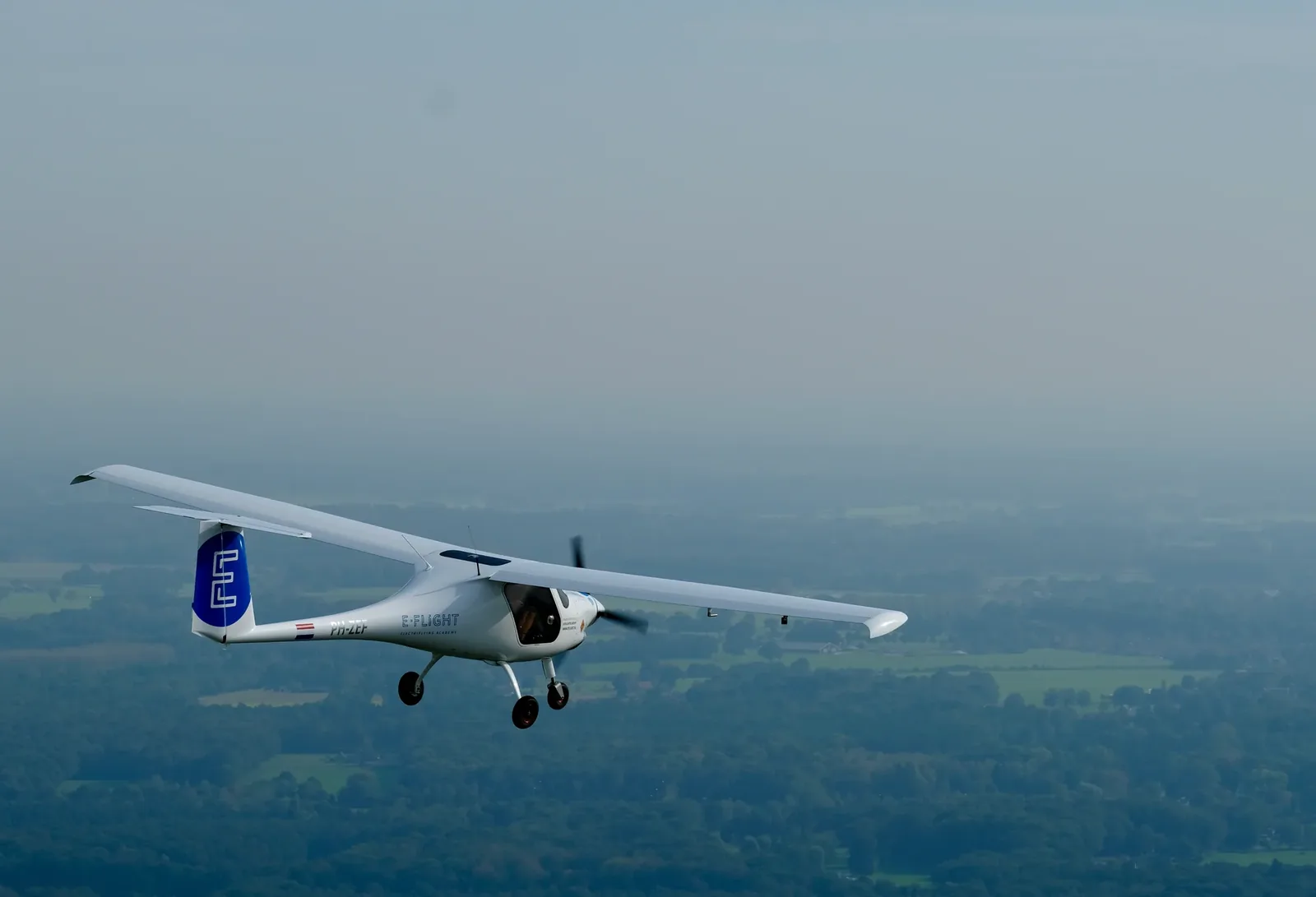 An E-Flight Academy electric training plane in flight over green fields.